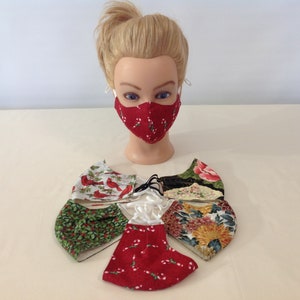 May include: A set of six face masks with various holiday-themed patterns. The masks are made of fabric and have adjustable ear loops. The patterns include red and white candy canes, cardinals on a white background, green holly leaves, and floral designs.