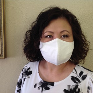 May include: A woman wearing a white face mask with a white and black floral print blouse.