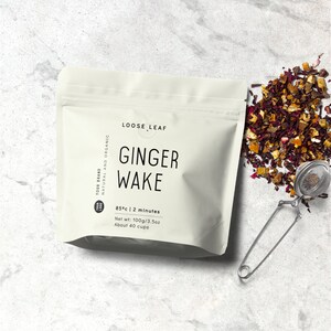 Op de afbeelding: Een witte zak met de tekst "LOOSE LEAF GINGER WAKE" erop gedrukt. De zak bevat losse thee en heeft instructies voor het zetten: 85 &deg;C | 2 minuten. Nettogewicht: 100 g/3,5 oz. Ongeveer 40 kopjes.