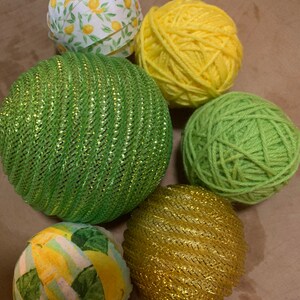 May include: Six balls of yarn in various colors and textures. The balls are green, yellow, gold, and white with a lemon print.