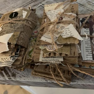 May include: A stack of vintage paper ephemera with brown paper, lace, and twine. The paper has text including "Sporting Goods/Hunting" and "Sept. Equip & Tools".