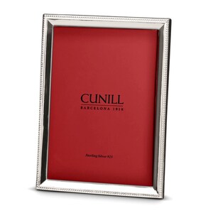May include: A silver picture frame with a beaded border and a red mount. The frame has the text "CUNILL BARCELONA 1916" and "Sterling Silver 925" printed on the mount.