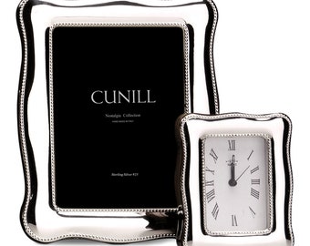Può includere: Due cornici per foto in argento con un bordo perlato. La cornice più grande ha uno sfondo nero con il testo "CUNILL Nostalgia Collection HAND MADE IN ITALY Sterling Silver 925". La cornice più piccola ha un quadrante dell'orologio bianco con numeri romani.