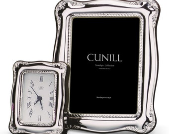 Può includere: Due cornici per foto placcate in argento con disegni decorativi. La cornice più grande ha uno sfondo nero con il testo "CUNILL Nostalgia Collection Hand Made in Italy Sterling Silver 925". La cornice più piccola ha un quadrante dell'orologio con numeri romani.