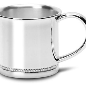 Peut inclure: Une tasse à bébé en argent avec un bord perlé. La tasse a une poignée arrondie.