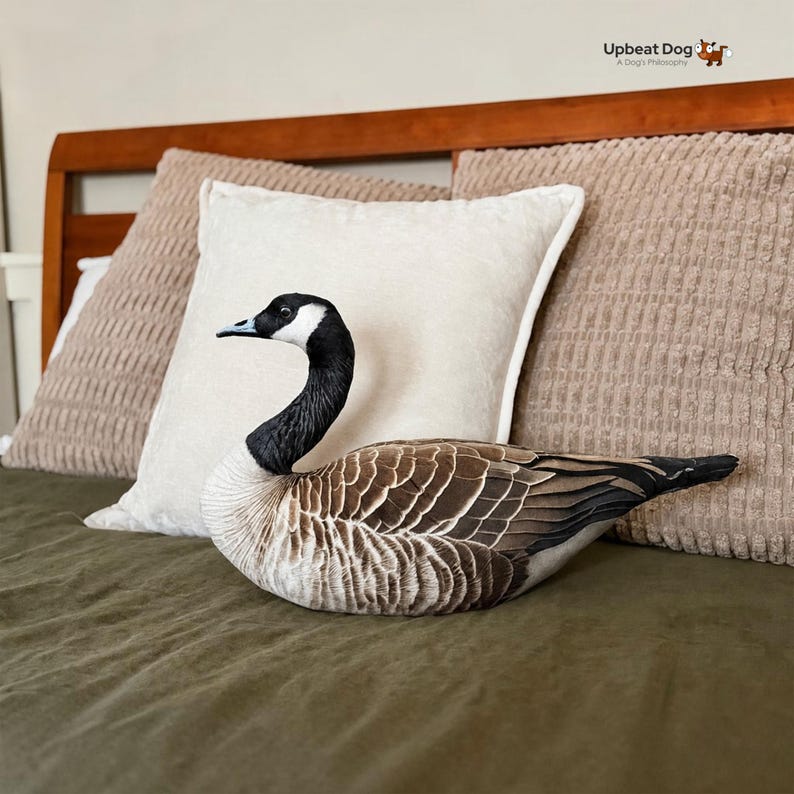 May include: A plush throw pillow shaped like a Canada goose with realistic brown, black, and white feather patterns. The goose has a black neck and head with a white cheek patch, a black beak, and a detailed wing design. The text Upbeat Dog A Dog's Philosophy is visible in the top right corner.