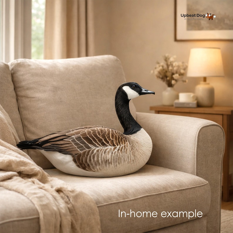 May include: A plush Canada goose toy featuring a black head and neck with a white cheek patch, a brown and tan patterned body, and a white underside. The goose is depicted in a resting position with its head held upright and alert.