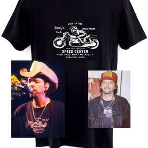 Peut inclure: T-shirt noir avec un graphique blanc d'une moto et le texte "Jenny's Cycle, Pro-Elim, Race Parts, 1974 race champion, Speed Center, "We Race What We Sell", Wenatchee, Wash."