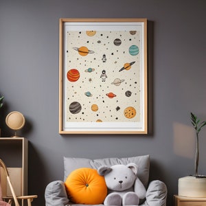 Puede incluir: Un sillón infantil gris con un cojín de respaldo gris y blanco con estampado y un oso de peluche gris. El sillón está en una habitación con una pared gris, una estantería de madera y una impresión enmarcada de planetas y estrellas.