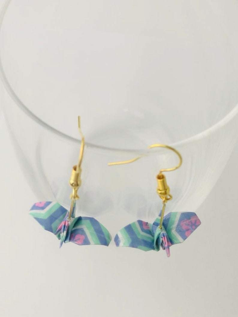 May include: A pair of origami crane earrings with a blue, green, and pink patterned design. The earrings are made with gold-colored hooks.