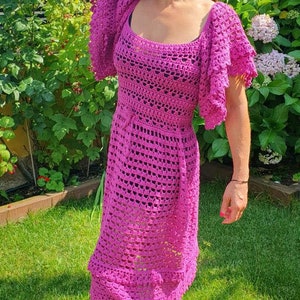 May include: A pink crochet dress with a square neckline and short, ruffled sleeves. The dress is fitted at the waist and flows out to a midi length.