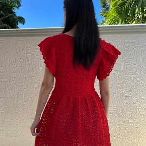 May include: A red crochet dress with a scalloped hem and short sleeves. The dress is made with a delicate openwork pattern.