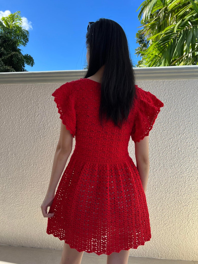 May include: A red crochet dress with a scalloped hem and short sleeves. The dress is made with a delicate openwork pattern.