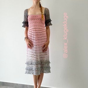May include: A pink and gray crochet dress with a square neckline and short sleeves. The dress has a tiered skirt and is made with a delicate openwork stitch. The dress is shown on a model with a braid in her hair. The image includes the text "@alex_klugekluge".