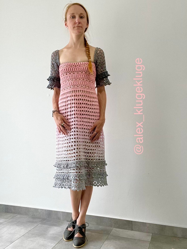 May include: A pink and gray crochet dress with a square neckline and short sleeves. The dress has a tiered skirt and is made with a delicate openwork stitch. The dress is shown on a model with a braid in her hair. The image includes the text "@alex_klugekluge".