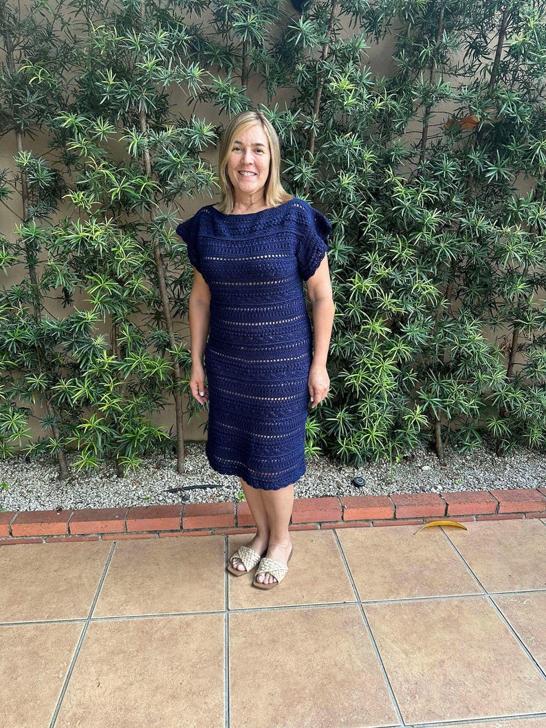 May include: A navy blue crochet dress with a loose fit and short sleeves. The dress has a simple design with horizontal stripes and a slightly flared skirt.