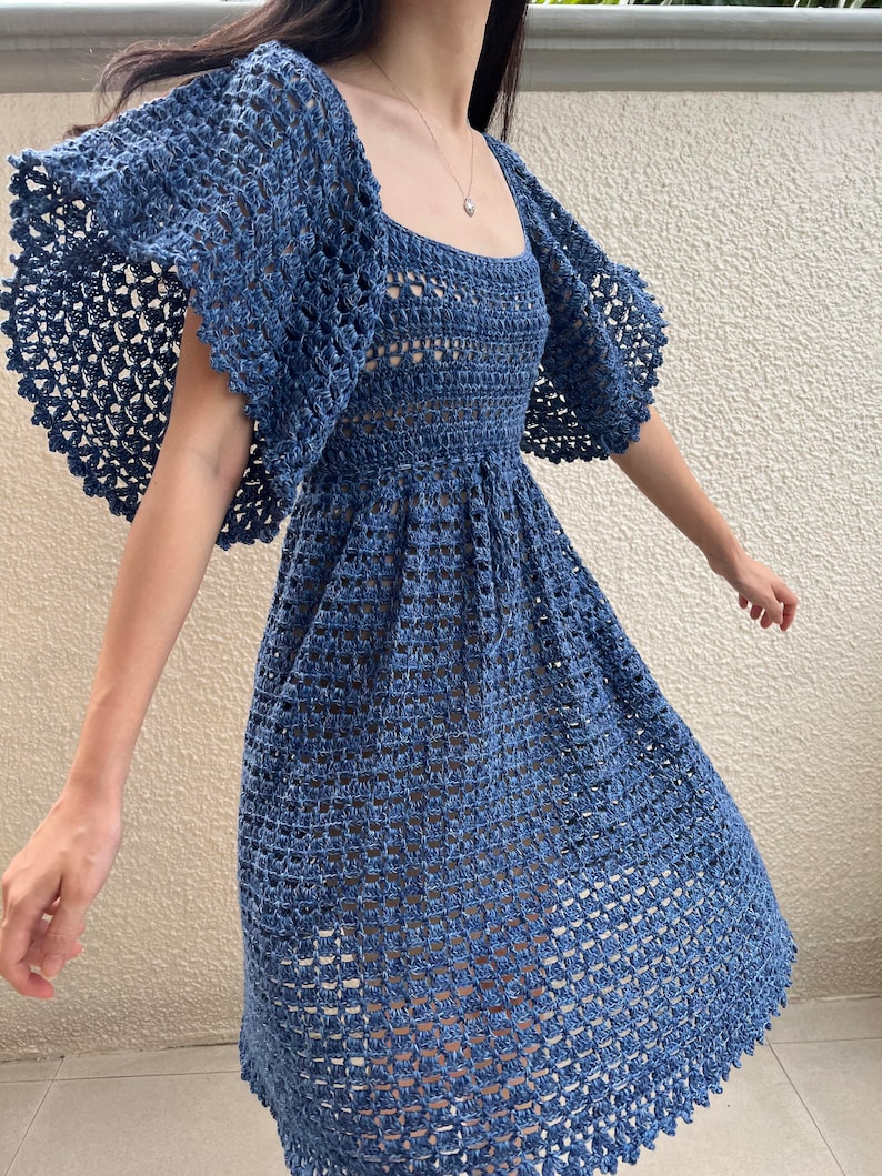 May include: A blue crochet dress with a square neckline and short, ruffled sleeves. The dress has a fitted bodice and a flowing skirt.