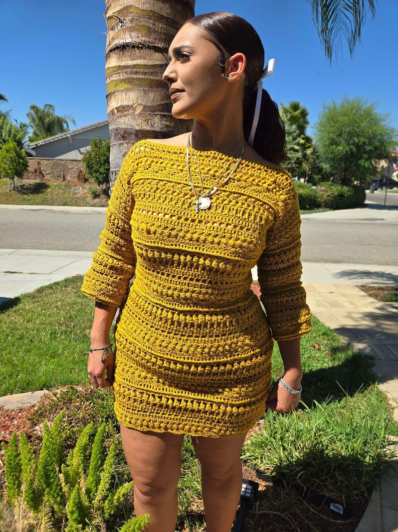 May include: A mustard yellow crochet dress with a scoop neckline and three-quarter sleeves. The dress is fitted and has a slightly flared skirt.
