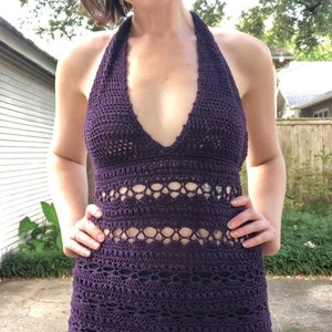 May include: A purple crochet halter dress with a black crochet trim. The dress has a deep V-neckline and a fitted silhouette.