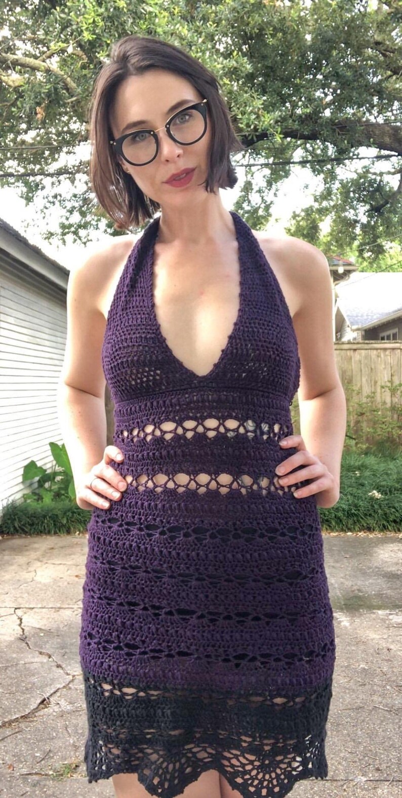 May include: A purple crochet halter dress with a black crochet trim. The dress has a deep V-neckline and a fitted silhouette.