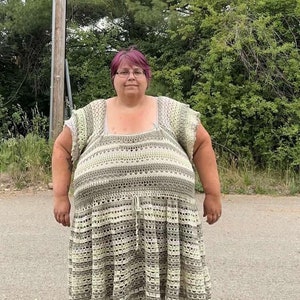 May include: A woman wearing a crocheted dress with a green and white striped pattern. The dress has a scoop neck and short sleeves. The woman has pink hair and is wearing glasses.
