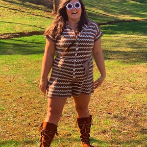 May include: A woman wearing a brown and white striped crochet dress with a brown belt, white daisy-shaped sunglasses, and brown leather boots with fringe.