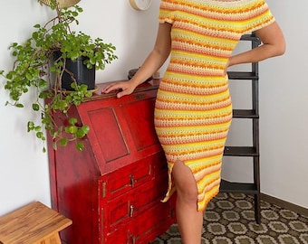 May include: A woman wearing a yellow, orange, and pink striped crochet dress with a side slit. The dress has an off-the-shoulder neckline and short sleeves.