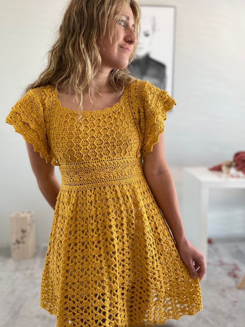 May include: A yellow crochet dress with a square neckline and short, ruffled sleeves. The dress has a fitted bodice and a flowing skirt.
