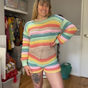K&ouml;nnte beinhalten: Ein farbenfrohes H&auml;kel-Set aus Pullover und Shorts. Der lang&auml;rmlige Pullover und die Shorts haben horizontale Streifen in Gelb-, Rosa-, Gr&uuml;n- und Blaut&ouml;nen. Die Shorts haben einen Kordelzug in der Taille. Das Set ist handgefertigt.
