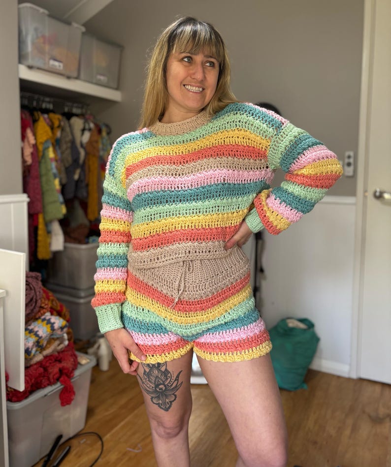 K&ouml;nnte beinhalten: Ein farbenfrohes H&auml;kel-Set aus Pullover und Shorts. Der lang&auml;rmlige Pullover und die Shorts haben horizontale Streifen in Gelb-, Rosa-, Gr&uuml;n- und Blaut&ouml;nen. Die Shorts haben einen Kordelzug in der Taille. Das Set ist handgefertigt.