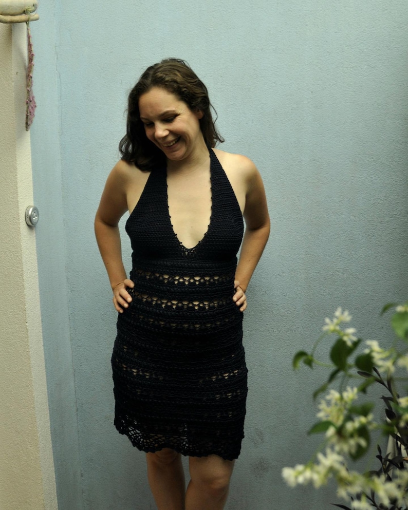 May include: A woman wearing a black crochet dress with a halter neckline. The dress has a fitted bodice and a flowing skirt.