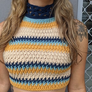 Op de afbeelding: Een gehaakt haltertop met een hoge halslijn en een gestreept patroon in beige, mosterdgeel, blauw en donkerblauw.