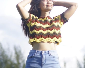 May include: A woman wearing a brown, yellow, and green striped crochet crop top with blue jeans.