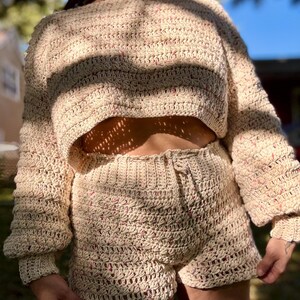 K&ouml;nnte beinhalten: Beige geh&auml;keltes zweiteiliges Set, bestehend aus einem cropped Pullover mit langen &Auml;rmeln und einer Shorts. Das Set hat eine strukturierte Masche mit rosa Tupfen. Die Shorts haben einen Kordelzug in der Taille.