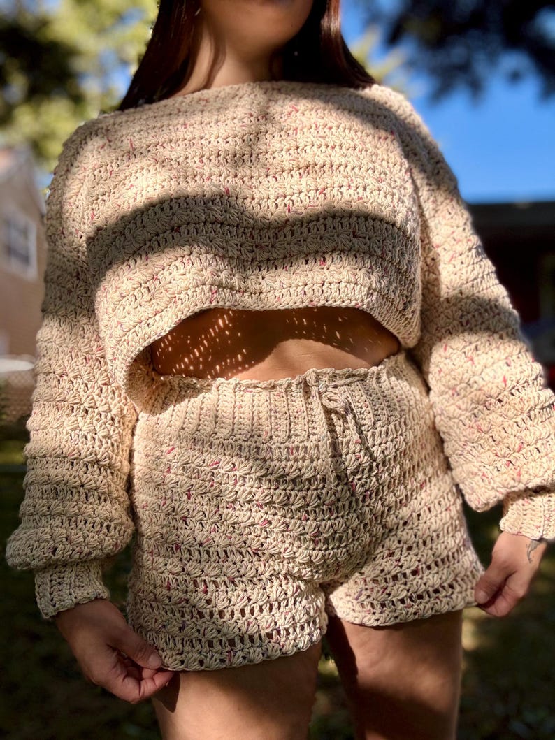 K&ouml;nnte beinhalten: Beige geh&auml;keltes zweiteiliges Set, bestehend aus einem cropped Pullover mit langen &Auml;rmeln und einer Shorts. Das Set hat eine strukturierte Masche mit rosa Tupfen. Die Shorts haben einen Kordelzug in der Taille.