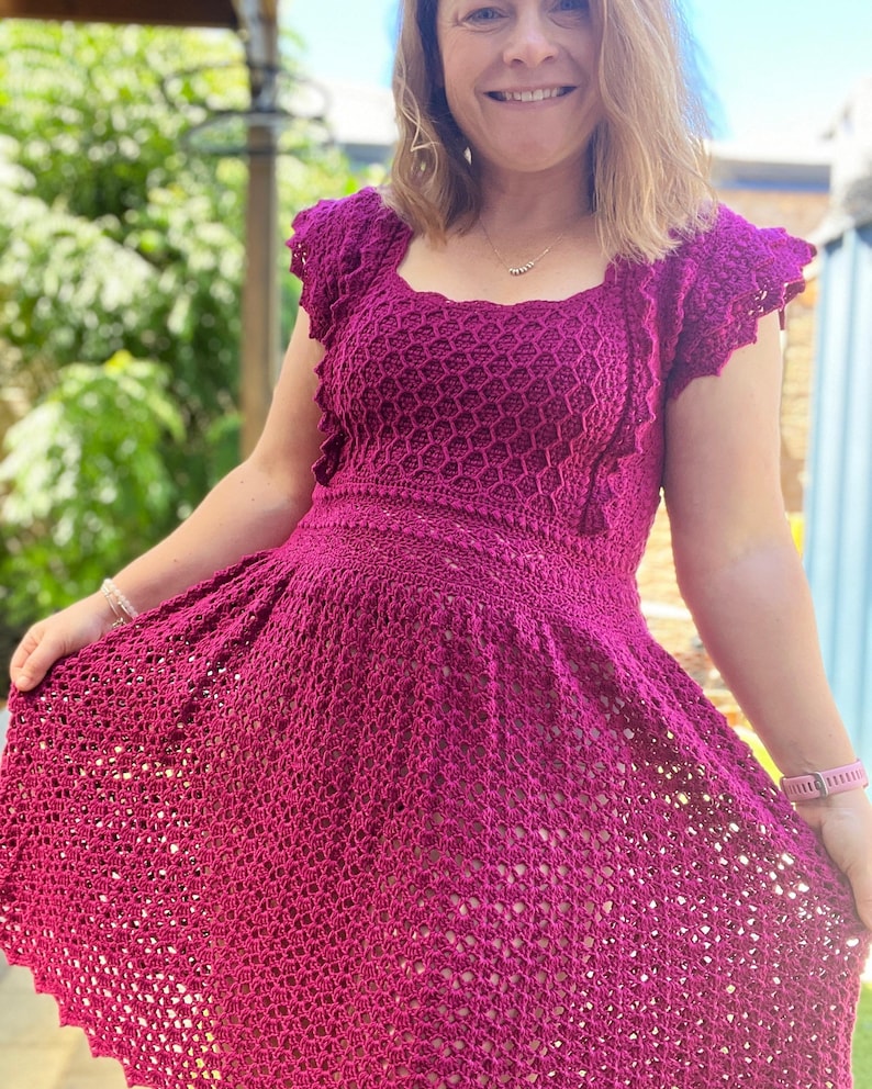 May include: A magenta crochet dress with a square neckline and short, ruffled sleeves. The dress has a fitted bodice and a flowing skirt.