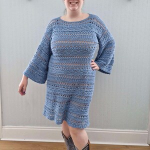 May include: A light blue crochet dress with a loose fit and bell sleeves. The dress is made with a delicate open stitch pattern and has a slightly flared hemline.