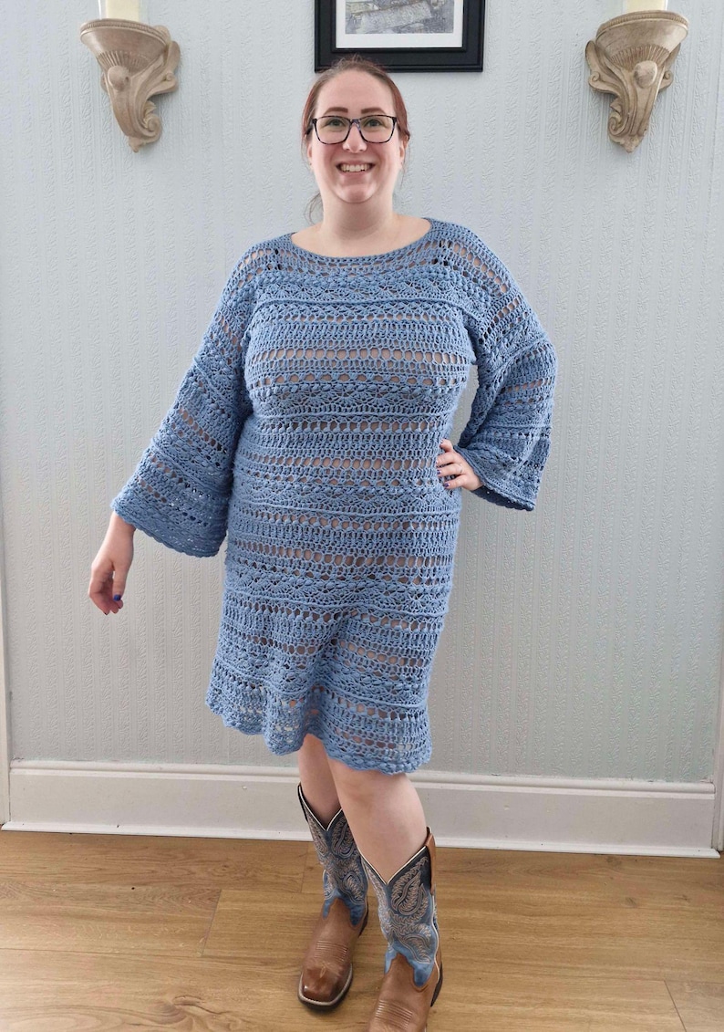 May include: A light blue crochet dress with a loose fit and bell sleeves. The dress is made with a delicate open stitch pattern and has a slightly flared hemline.