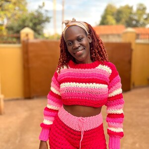 K&ouml;nnte beinhalten: Handgefertigtes H&auml;kel-Crop-Top und Shorts-Set in Rosa- und Wei&szlig;t&ouml;nen. Das Oberteil hat horizontale Streifen, w&auml;hrend die Shorts einen Kordelzug in der Taille haben. Ein farbenfrohes Beispiel f&uuml;r H&auml;kelbekleidung.