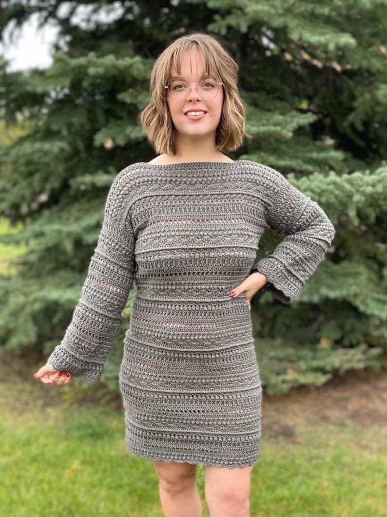 May include: A grey crochet dress with long sleeves and a slightly flared skirt. The dress has a textured pattern and a loose fit.