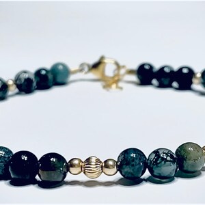 May include: A green and black gemstone bracelet with gold accents. The bracelet is made of round beads and has a clasp closure.