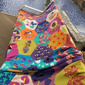 May include: A colorful knitted throw blanket with a hexagonal pattern featuring various nature-inspired designs, including bees, flowers, and leaves.