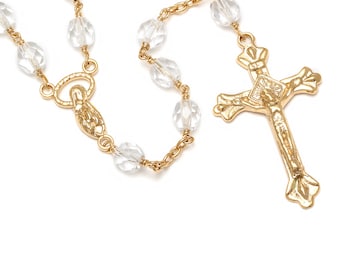 Può includere: Un rosario d'oro con perline di vetro trasparente e un crocifisso d'oro. Il crocifisso presenta una raffigurazione di Gesù Cristo.