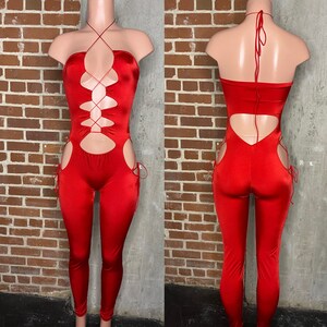 May include: Red jumpsuit with a lace-up design and cutouts on the front and sides. The jumpsuit has a halter neck style and is made of a stretchy fabric.