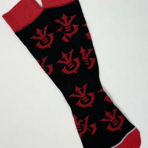 May include: A pair of black socks with red cuffs and toes. The socks feature a repeating red graphic pattern. A thin silver stripe accents the heel.