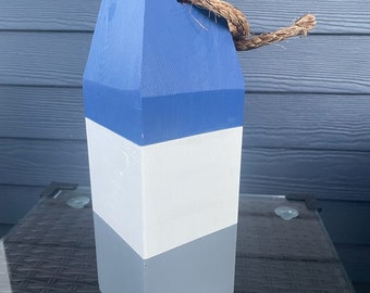 Peut inclure: Une bouée nautique en bois bleu, blanc et gris avec une boucle de corde. La bouée est un objet décoratif pour une maison à thème nautique.