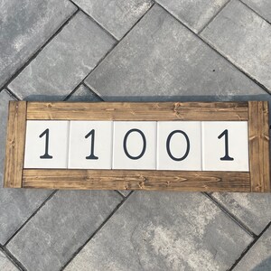 May include: A wooden sign with white tiles displaying the number 11001. The sign is made of dark brown wood and has a rustic look.