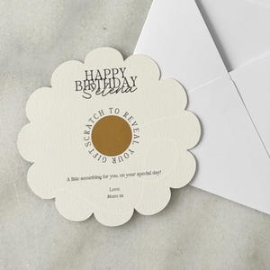 May include: A white envelope with a matching, flower-shaped scratch-off card. The card has the text "Happy Birthday Selena" and "Scratch to Reveal Your Gift". The card is cream-colored with a gold scratch-off area.