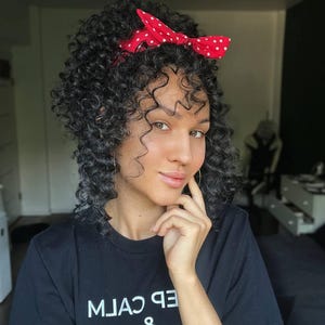 May include: A black t-shirt featuring white text that reads "KEEP CALM & CARRY ON" in a stacked format. The garment is worn with a bright red headband decorated with small white polka dots, which is tied in a bow at the top of the head.