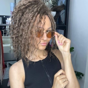 Könnte beinhalten: Eine Sonnenbrille mit rundem Rahmen, dünnen goldfarbenen Metallrändern und bernsteinfarbenen Gläsern. Die Sonnenbrille verfügt über einen klassischen Steg und schmale Bügel, die einen klaren Blick auf die runden Rahmen und die Tönung ermöglichen.